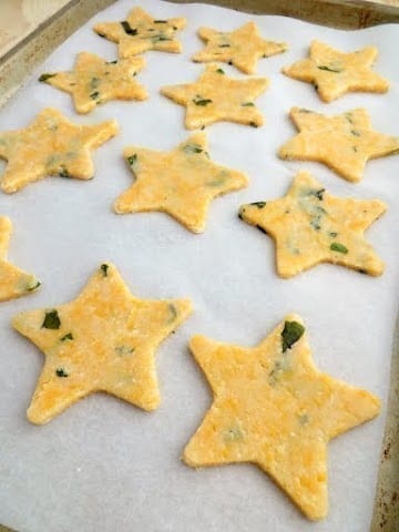 12 uncooked parmesan, basil, and cheddar bites laying on a parchment paper lined baking tray.
