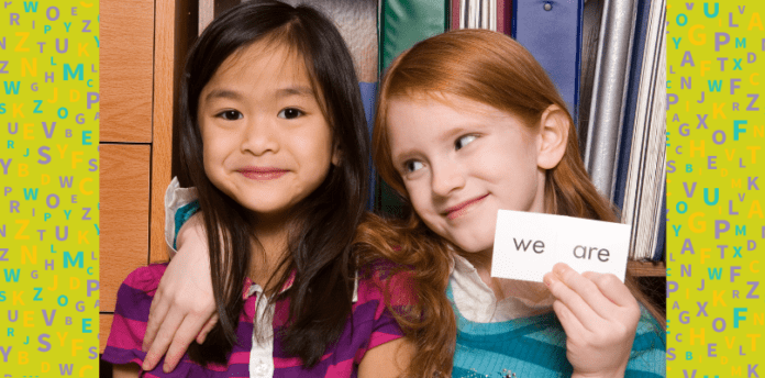 Two girls smiling and holding a card that says "WE"