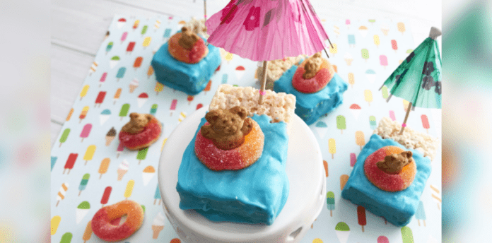 Floating Rice Krispie treats with teddy bears. Half of the treat is covered in blue icing and on top of the blue is a gummy ring with a grahams teddy sitting inside.