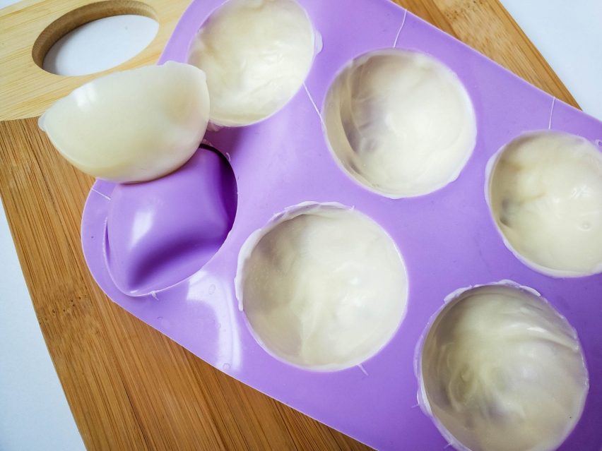 white chocolate cocoa bombs half-spheres with one pushed out of the silicone mold. 