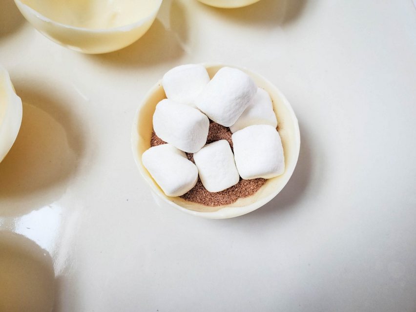 A white chocolate cocoa bomb half-sphere filled with milk chocolate cocoa mix and mini marshmallows.