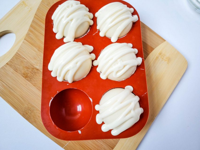 Five white chocolate cocoa bombs with white chocolate zig-zags across the top.