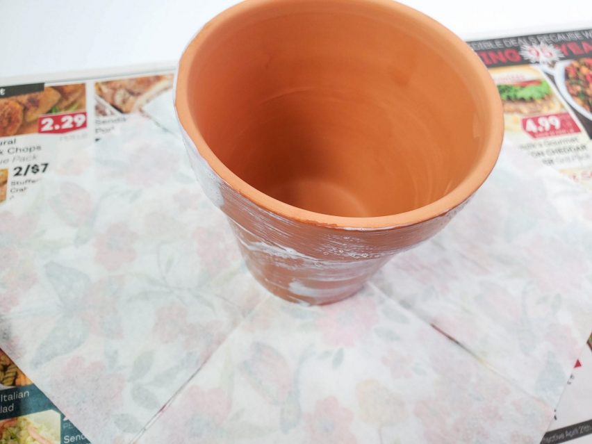 The second step in creating a decoupage flower pot. A terracotta flower pot standing at the center of an unfolded, face down paper napkin.