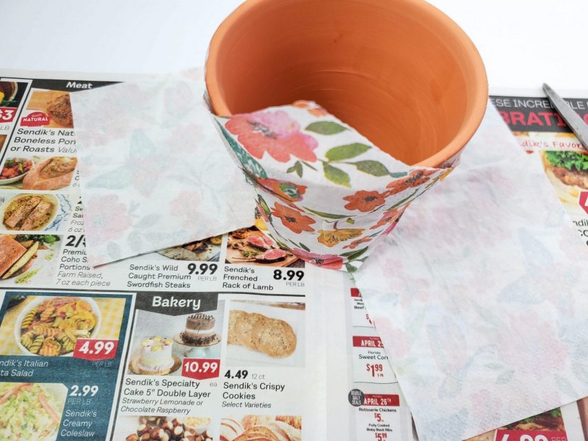 Decoupage flower pot part way through creation. A paper napkin is smoothed against the outside and the tip of the napkin is folded against the rim.