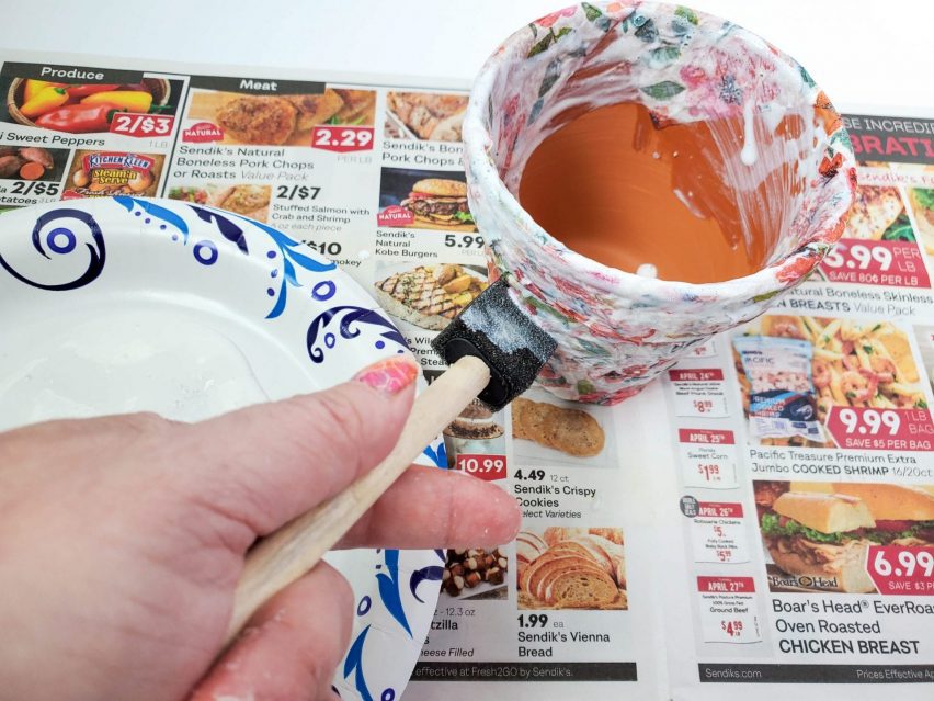 Decoupage flower pot craft step one. Applying a layer of Mod Podge to the outside surface of a flower pot, using a foam brush.