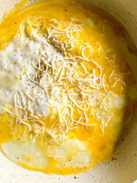 Cooked, beaten egg on the bottom of a frying pan with shredded cheese on top.