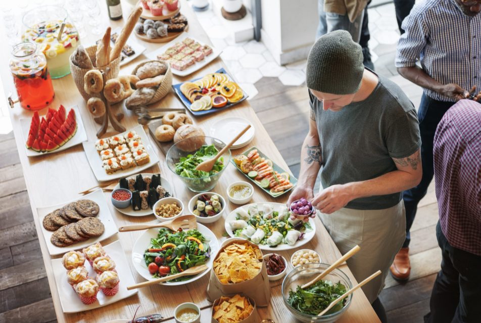 Young man standing at a fully laden, wooden buffet table, choosing between salads, fish, and cookies